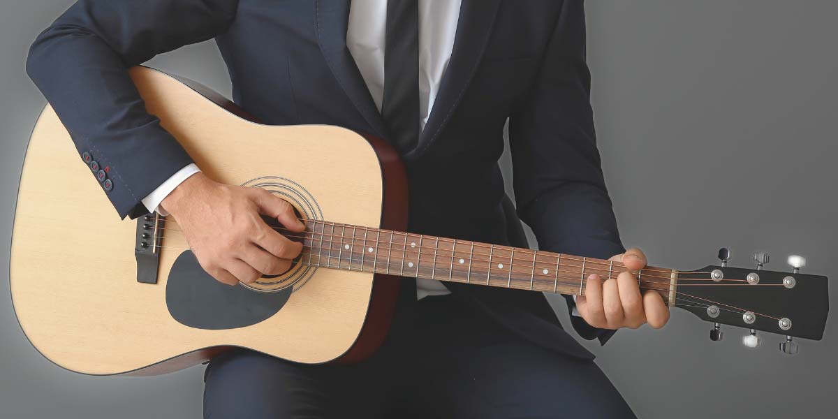 a man in a business suit strums an acoustic guitar to highlight the point of keeping sales kills in tune